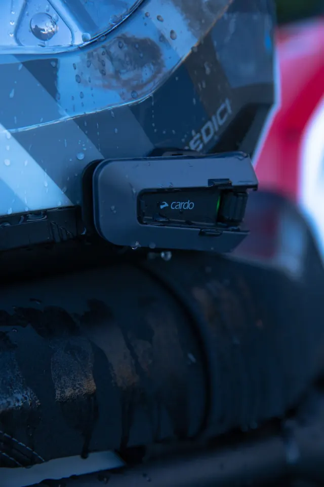 Cardo Packtalk Edge mounted on a rain-covered motorcycle helmet