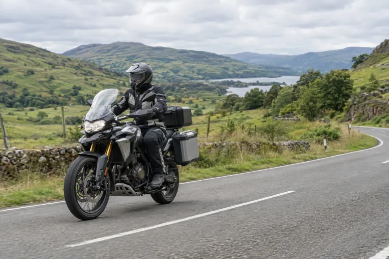 Motorcyclist riding through green hills beside a lake