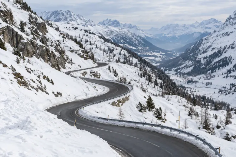 Winding cleared mountain road between snow-covered alpine slopes