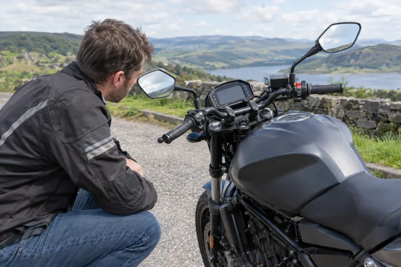 Rider looking at a parked motorcycle beside a country road