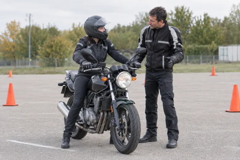 Instructor speaking with a rider on a stationary motorcycle at a training area