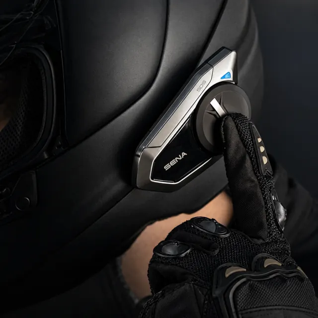 Sena 50S communicator attached to a helmet beside a gloved hand
