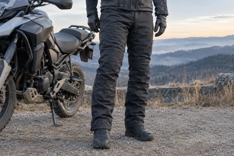 Insulated riding trousers and boots beside a parked motorcycle